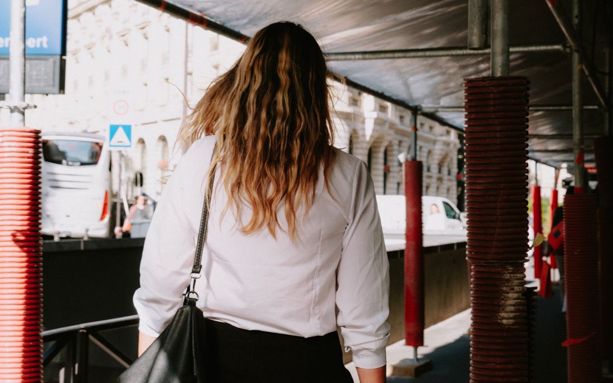 Rear view of woman in white shirt walking under scaffolding on a city street.