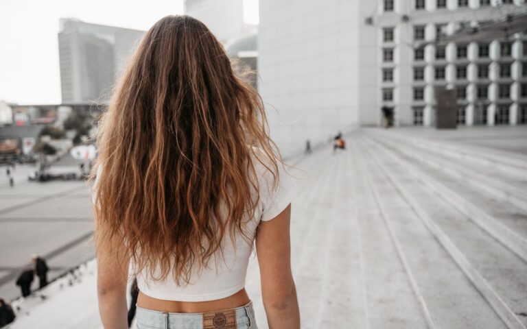 Woman with long brown hair walking up concrete steps in an urban setting.