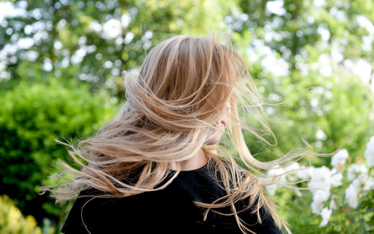 Blonde woman outside with hair blowing in the wind on a sunny summer day.