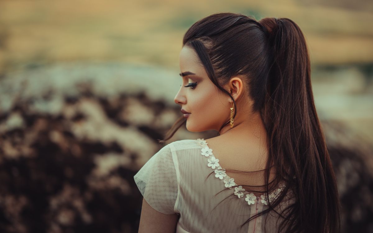 A stylish woman with long brown hair wearing a white dress, shot from behind outdoors in Moscow, Russia.