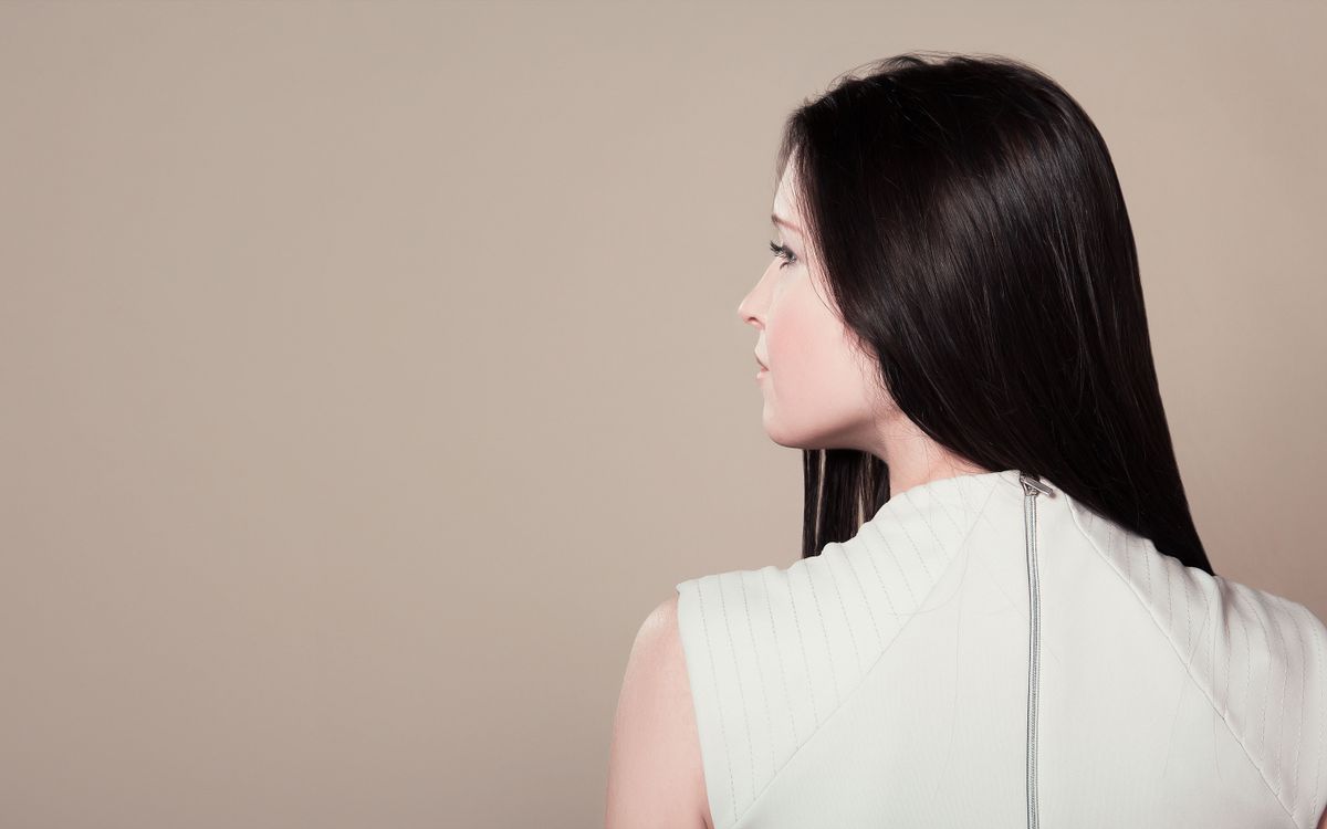 Profile view of a brunette woman in white attire indoors on a neutral background.