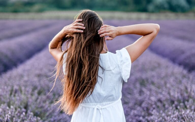 Back view of a woman in a white dress surrounded by lavender, enjoying nature.