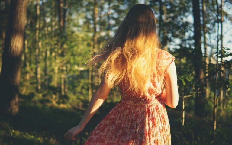 A woman in a floral dress walks through a sunlit forest. Bright back view.