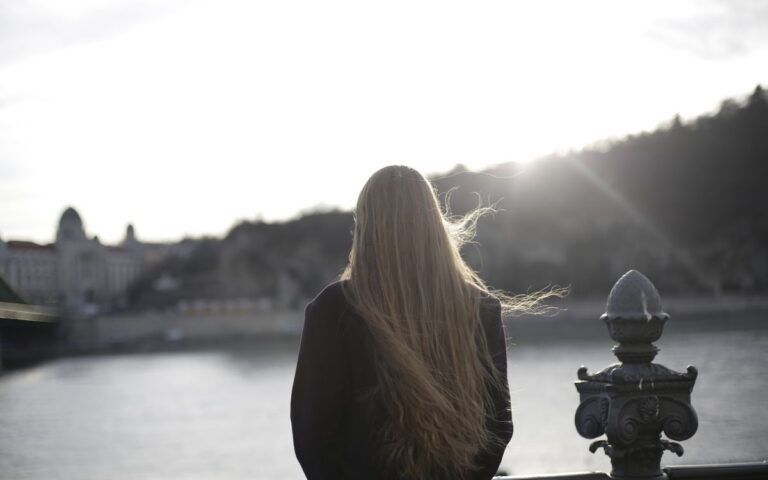 Back view of woman in violet coat contemplating a scenic riverside during sunset.