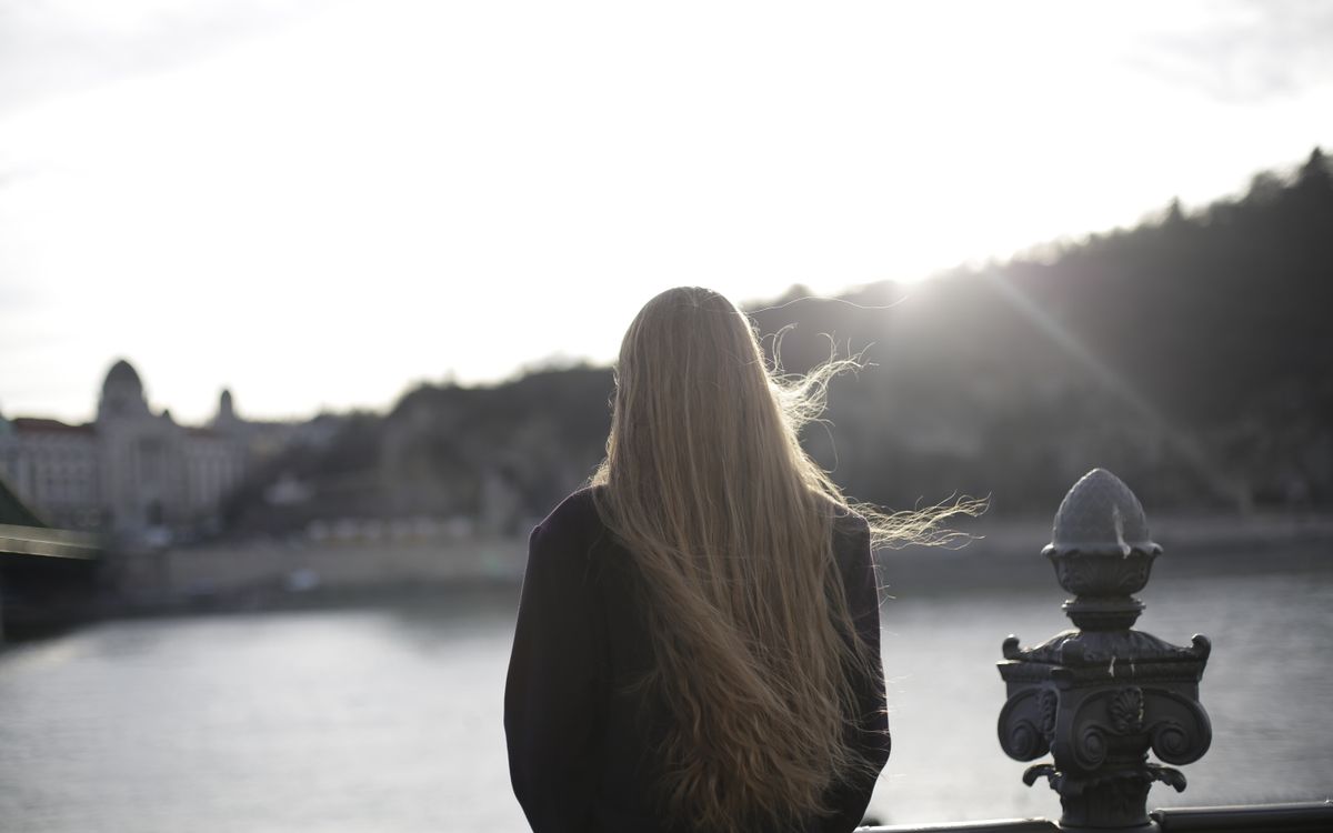 Back view of woman in violet coat contemplating a scenic riverside during sunset.