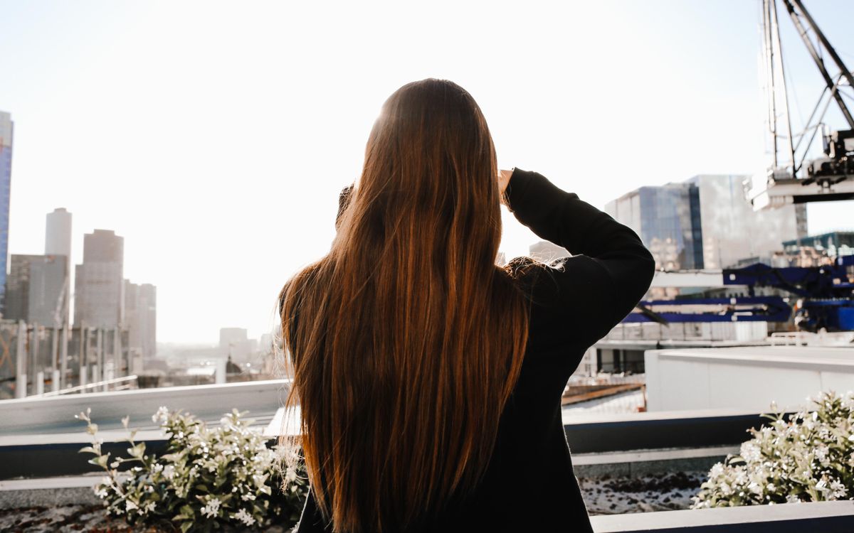 Rear view of a woman with long brown hair observing a city skyline. Bright and modern urban scene.