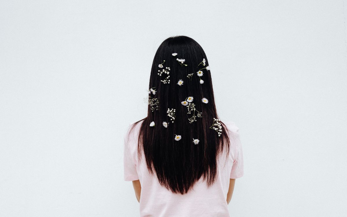 Back view of a woman with long hair adorned with small flowers on a white background.
