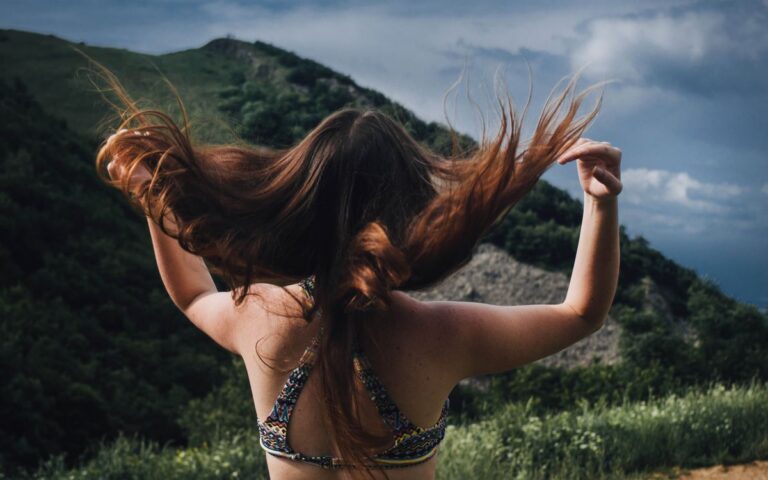 A woman flipping her hair in front of a lush green mountain landscape.