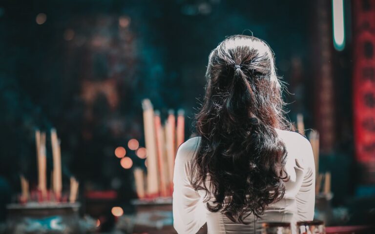 A woman with long hair is seen from behind praying inside a Vietnamese temple, surrounded by incense.