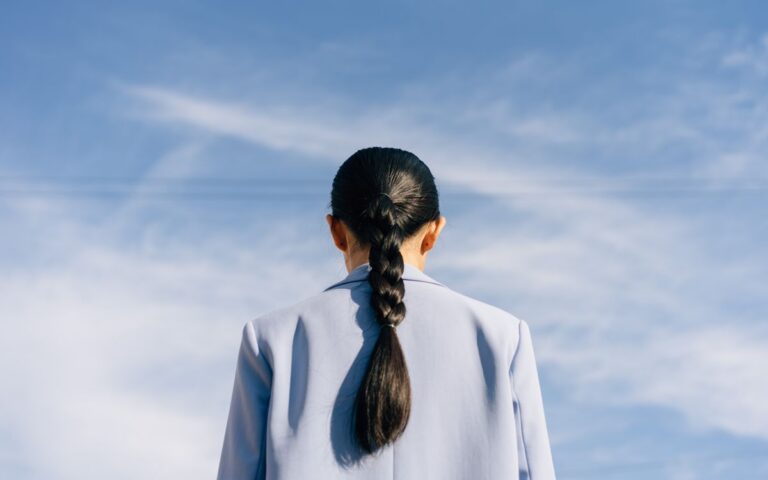 Back view of a woman with a braid against a vibrant blue sky. Ideal for concepts of freedom and aspiration.