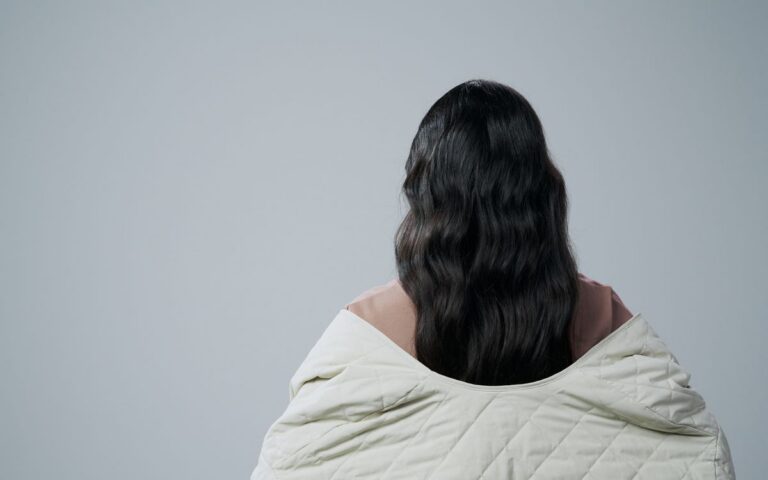 Rear view of woman with long hair wrapped in a blanket against a gray background, offering copy space.