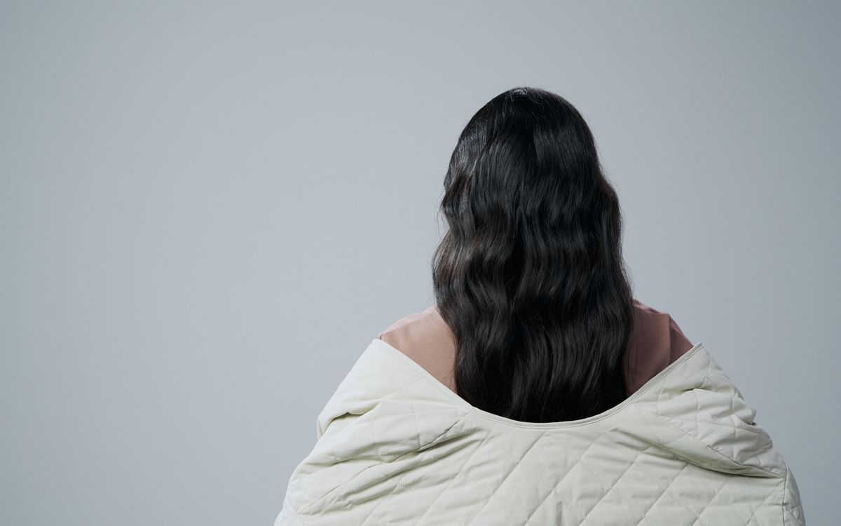 Rear view of woman with long hair wrapped in a blanket against a gray background, offering copy space.