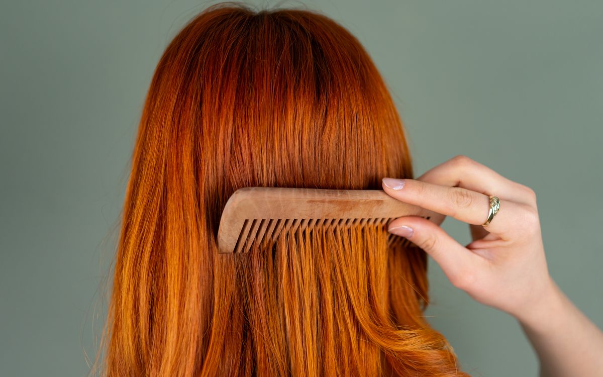 Close-up of a woman's red hair being combed with a wooden comb, capturing the smooth texture.
