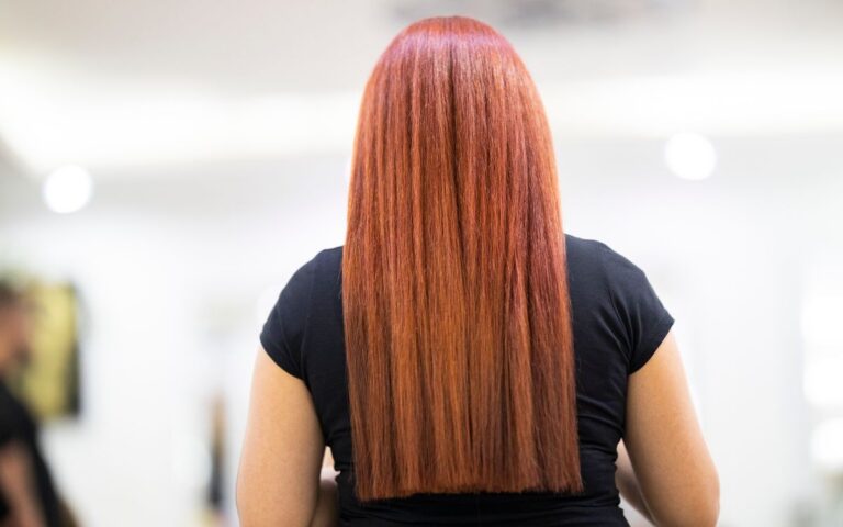 A woman with straight, vibrant red hair seen from the back, showcasing a fresh hairstyle in a professional salon.