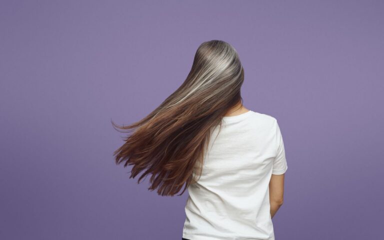 Rear view of a woman with long, flowing gray hair against a purple backdrop.