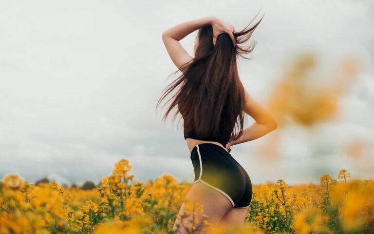 A woman in a black outfit enjoying a vibrant field of yellow flowers with a gentle breeze.